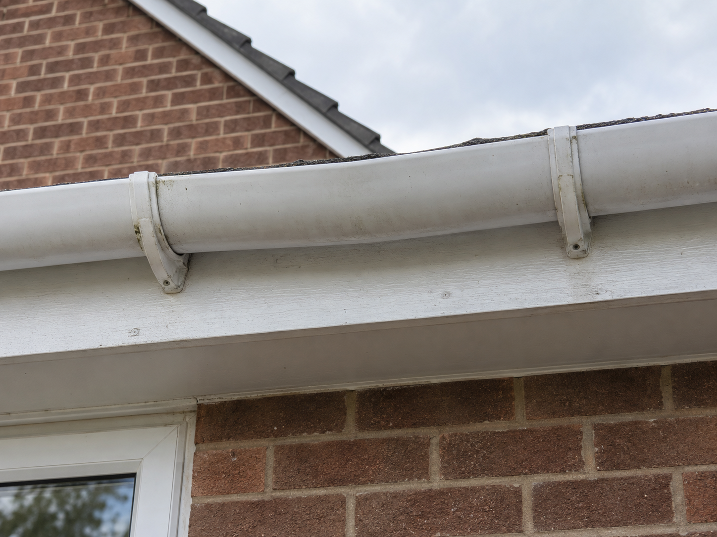 Loose gutter brackets and a low spot along a white uPVC gutter run